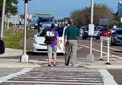 Image shows 2 people, Jen Graham COMS and Jeff Thompson PE with their backs to the camera and in motion, walking through a street-level opening in the island and approaching the separate right-turning lane.